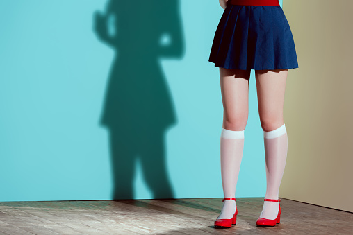 cropped shot of girl in red shoes, stockings and skirt posing in studio